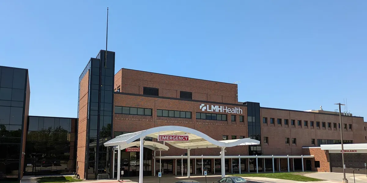 The emergency entrance of a hospital, with a white curved canopy over the doors and an ambulance bay alongside