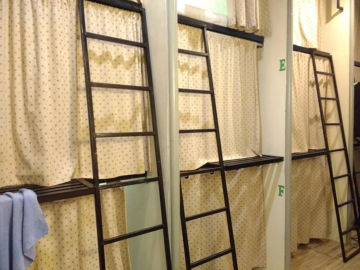 Metal bunk-bed ladders beside bunks screened by patterned privacy curtains in a hostel dormitory