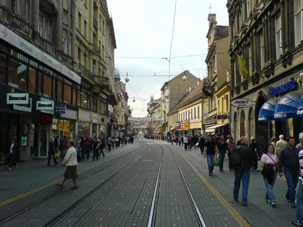A European city street with tram tracks curving into the distance, lined with shopfronts