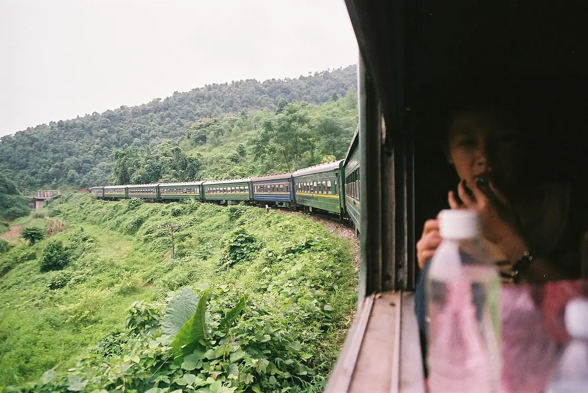 A train curving through green hillside vegetation, seen from a carriage window